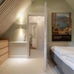 Schlafzimmer mit Dachschrägen, Bett und Kleiderschrank. Tür führt in Bad.