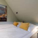 Schlafzimmer mit Dachschräge, Bett mit gelben Kissen und Wandbild.