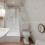 Badezimmer mit Dusche, Waschbecken und Toilette. Weiße Fliesen und Holzboden.