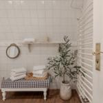 Badezimmer mit weißen Fliesen, Holzboden, Toilette, Spiegel und Pflanze.
