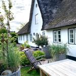 Haus mit strohgedecktem Dach und Gartenbereich mit Holztisch und Liegestuhl.