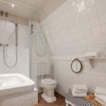 Badezimmer mit Dusche, Waschbecken und Toilette. Weiße Fliesen und Holzboden.