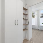 Schlafzimmer mit weißen Schränken und Holzregalen. Fenster mit Vorhängen und Pflanze.