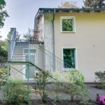 Haus mit Balkon, Treppe und Garten. Fenster mit weißen Rahmen.