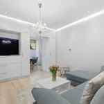 Wohnzimmer mit grauem Sofa, weißem Couchtisch und integriertem Fernseher.