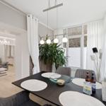 Esstisch mit Stühlen und Fensterblick. Wohnzimmer im Hintergrund.