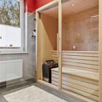 Sauna mit Holzbänken und Glaswand. Fenster mit Jalousie. Fliesenboden und Teppich.