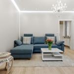 Ein Wohnzimmer mit blauem Sofa, weißem Couchtisch und Kronleuchter.