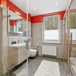 Badezimmer mit Dusche, Waschbecken und Toilette. Fenster mit Blick auf Wald.