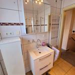 Helles Badezimmer mit Waschplatz, Dusche und ausreichend Stauraum.