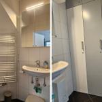 Badezimmer mit Waschbecken, Spiegel und Heizkörper. Nebenraum mit Schrank und Waschbecken.