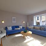 Zwei blaue Sofas, ein runder Tisch und ein weißer Stuhl im Wohnzimmer mit Blick auf den Garten.