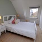 Schlafzimmer mit weißem Bett, Nachttisch und Fenster.