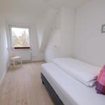 Schlafzimmer mit Bett, Schrank und Fenster. Holzboden und Wanddekoration.