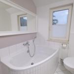 Badezimmer mit Badewanne, Spiegel und Toilette. Fenster mit Jalousie.