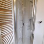 Dusche mit Glaswand und Duschbrause. Heizung und Badewanne sind sichtbar.
