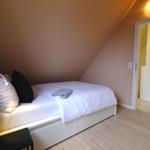 Schlafzimmer mit Bett, Kissen und Holzboden unter schräger Decke.