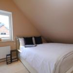 Schlafzimmer mit Dachschrägen, weißem Bett und Fenster mit Blick auf Dach.