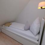 Schlafzimmer mit Dachschräge, weißem Bett und Wandlampe.