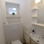 Badezimmer mit Waschbecken, Spiegel, Heizung und Toilette. Fenster mit Pflanze.
