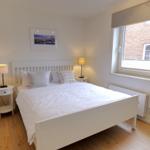 Schlafzimmer mit weißem Bett, zwei Nachttischen und Fenster.