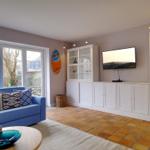 Ein Wohnzimmer mit blauem Sofa, TV und weißen Schränken.