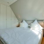 Schlafzimmer mit weißem Bett, Nachttischen und Schrank unter Dachschrägen.