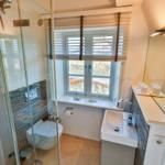 Badezimmer mit Dusche, Toilette und Waschbecken. Fenster mit Jalousie und Handtuchwärmer.