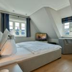 Schlafzimmer mit Bett, Schreibtisch und TV. Zwei Fenster mit Blick nach draußen.