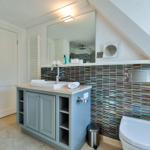 Badezimmer mit Waschbecken, Spiegel und Toilette. Wandverkleidung mit bunten Fliesen.