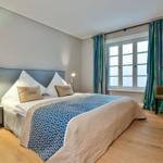Schlafzimmer mit Bett, Fenster, Vorhängen und Sessel.
