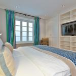 Schlafzimmer mit Bett, Fenster, Gardinen und TV-Wand.