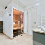 Dusche, Toilette und Sauna in einem Raum mit Glaswand und Holzbank.