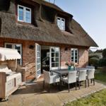 Haus mit Strohdach, Terrasse mit Esstisch und Liegestuhl.
