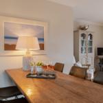 Dining table with chairs, lamp, and picture on the wall. In the background, a cabinet and TV are visible.