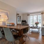Dining area with wooden table and chairs, living area with sofa and window to outdoor terrace.