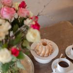 Table with coffee, cake, and floral arrangement.