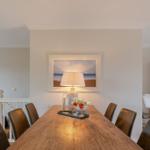 Dining room with wooden table, chairs, and wall art. Lamp and fruit bowl on table.