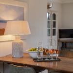 Wooden table with lamp, glasses, and fruit. Wall art and TV in background.