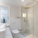 Bathroom with shower, sink, and toilet. White walls and marble tiles.
