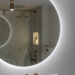 Shower cabin with marble wall and brass fixtures visible through round mirror.