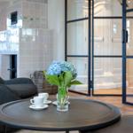 Round table with flowers and cups in front of a chair and fireplace.