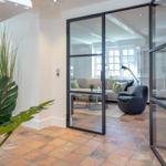 Glass wall separates entrance from living area with sofa and armchair.