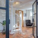 Entrance with white spiral staircase and terracotta floor. Dark armchair and glass walls.