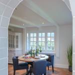 Dining room with round table, blue chairs, and terracotta floor under arched opening.