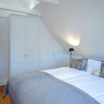 Bedroom with sloped ceiling, white wardrobe, and bed with gray blanket.