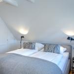 Bedroom with double bed, white walls, and sloped ceiling beams.