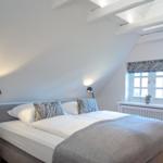 Bedroom with double bed, window, and wooden beams on the ceiling.