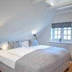 Bedroom with double bed, wooden floor, and sloped ceiling beams. Window with curtain.