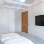 Bedroom with bed, wardrobe, and wall-mounted TV under sloped ceiling.